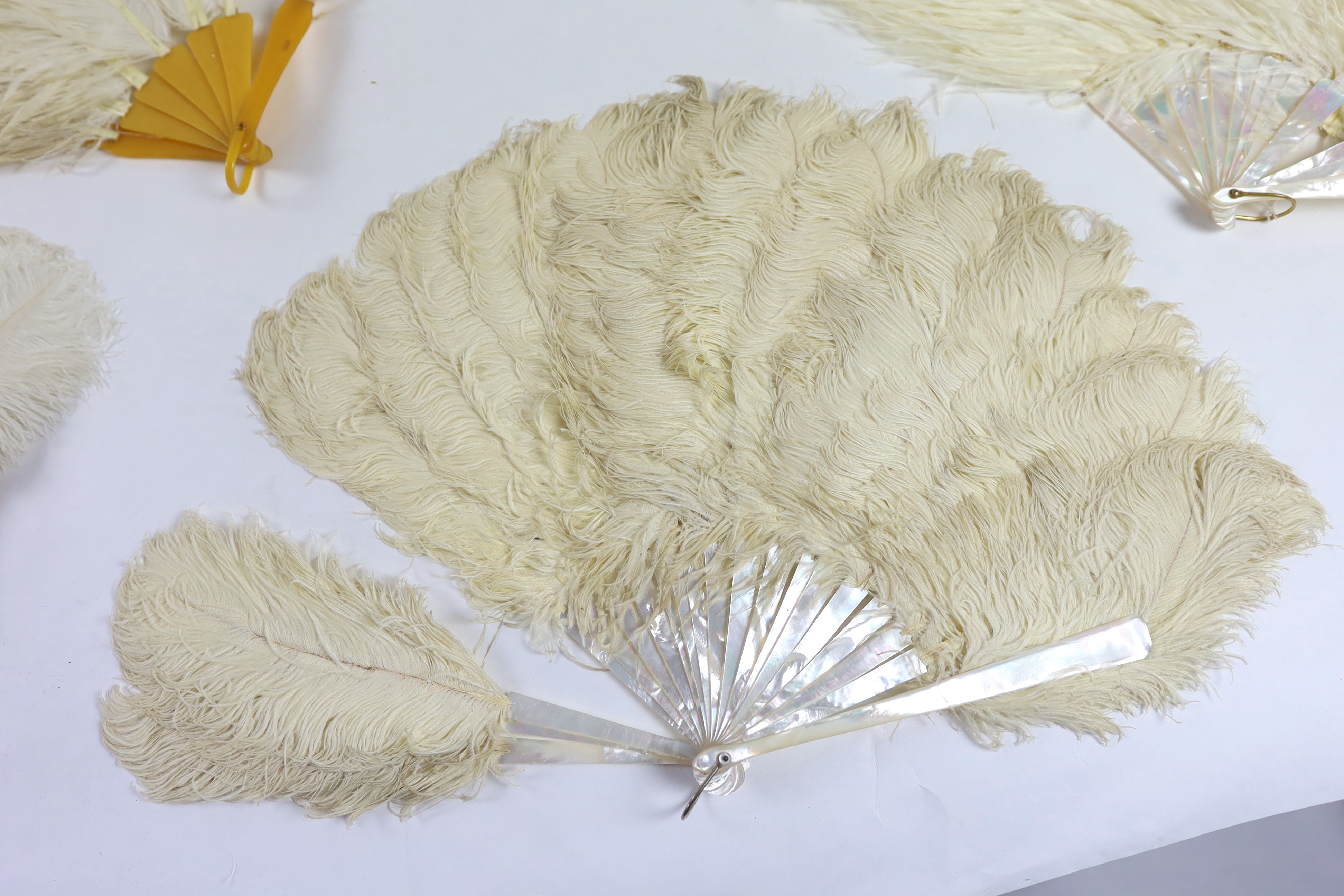 Two early 20th century Ostrich feather and mother of pearl fans, another similar fan with amber Bakelite handle and a small tortoiseshell and feather fan (4)